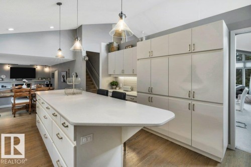 Kitchen featuring a large island with integrated storage, light-toned countertops, extensive cabinetry, wood-finish flooring, and recessed and pendant lighting - 11742 29 Avenue, Edmonton, AB 