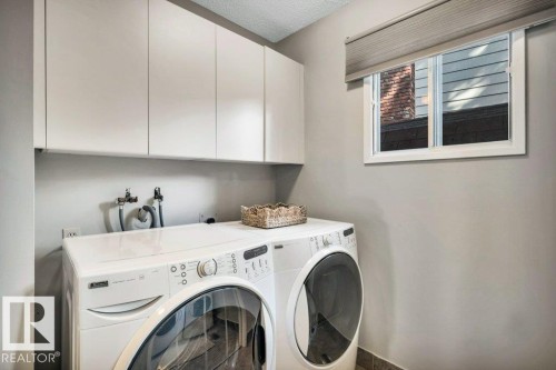 Dedicated laundry area featuring white wall cabinetry, a white window frame with a neutral-toned blind, and tile flooring - 11742 29 Avenue, Edmonton, AB 