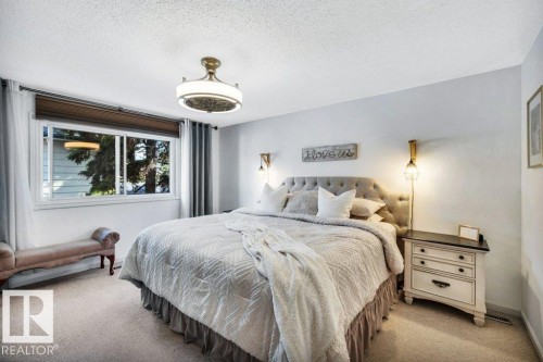 Spacious bedroom featuring light-colored carpeting, a large window with white framing, and a ceiling-mounted light fixture with a decorative drum shade - 11742 29 Avenue, Edmonton, AB 
