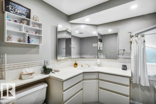 Bathroom featuring an integrated sink, corner vanity with white cabinetry, light-toned countertop, and tiled walls - 11742 29 Avenue, Edmonton, AB 