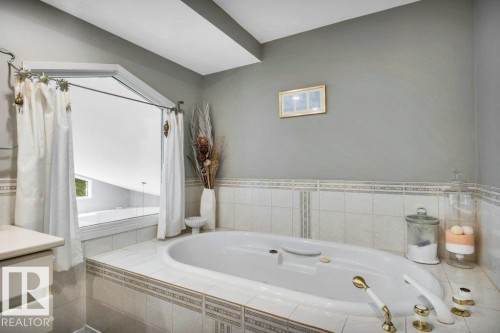 Soaking tub with gold-tone fixtures, surrounded by white tile and an accent border - 11742 29 Avenue, Edmonton, AB 