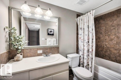 Bathroom featuring a white vanity with an integrated sink, a large framed mirror, and a three-light fixture - 11742 29 Avenue, Edmonton, AB 