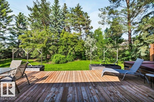 Expansive outdoor living area featuring a wood deck, lush green lawn, and mature trees - 11742 29 Avenue, Edmonton, AB 
