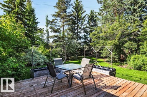 Expansive wood deck with a clear glass-top table, surrounded by mature trees and lush greenery - 11742 29 Avenue, Edmonton, AB 