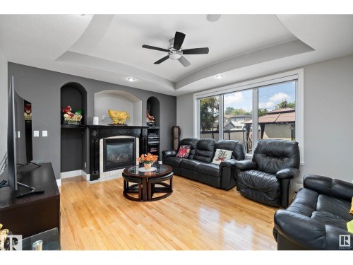 Living space featuring wood-finish flooring, a tray ceiling with a ceiling fan, and a prominent fireplace with a dark mantel - 9544 154 Street, Edmonton, AB 