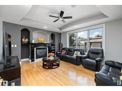 Living space featuring wood-finish flooring, a tray ceiling with a ceiling fan, and a prominent fireplace with a dark mantel - 