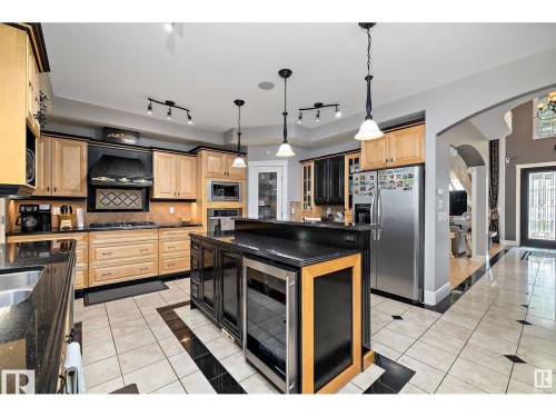 Gourmet kitchen featuring a central island with integrated beverage coolers, black countertops, and pendant lighting - 9544 154 Street, Edmonton, AB 
