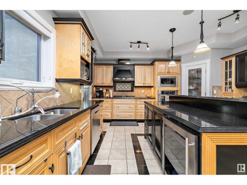 Kitchen featuring light wood cabinetry with dark trim, black countertops, and stainless steel appliances - 9544 154 Street, Edmonton, AB 