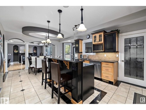 Spacious kitchen and dining area featuring a breakfast bar with seating for three, two-tone cabinetry with plate rack, stainless steel appliances, and a tiled backsplash - 9544 154 Street, Edmonton, AB 