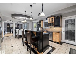 Spacious kitchen and dining area featuring a breakfast bar with seating for three, two-tone cabinetry with plate rack, stainless steel appliances, and a tiled backsplash - 