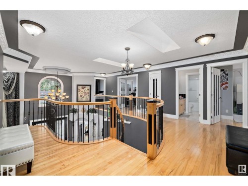 Upper-level landing featuring wood-finish flooring, a curved staircase with wrought iron balusters, cased door openings, and crown molding accents - 9544 154 Street, Edmonton, AB 