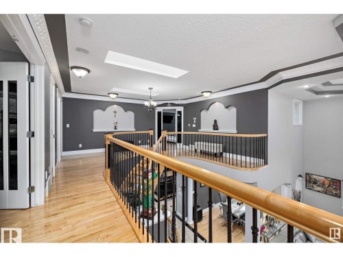 Upper-level hallway featuring wood-finish flooring, a decorative railing with black spindles and a light wood-finish handrail, architectural wall niches, a skylight, and tray ceilings with recessed lighting - 9544 154 Street, Edmonton, AB 
