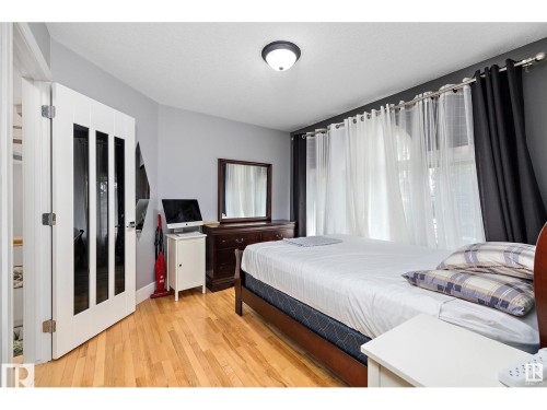 Spacious room featuring wood-finish flooring, a contemporary ceiling light fixture, and a white interior door with vertical glass inserts - 9544 154 Street, Edmonton, AB 