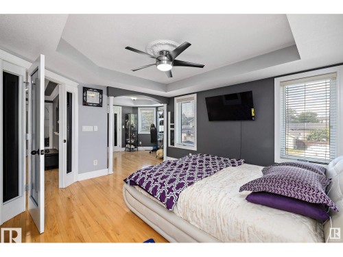 Bedroom featuring hardwood flooring, tray ceiling with a modern ceiling fan, multiple windows with blinds, and French doors - 9544 154 Street, Edmonton, AB 