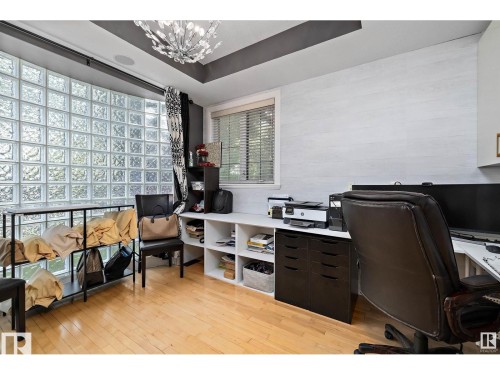 Room featuring a large glass block wall, wood-finish flooring, and built-in shelving and desk space - 9544 154 Street, Edmonton, AB 