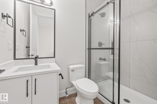 Modern bathroom featuring a glass-enclosed shower with white tiled walls, a white vanity with an integrated sink, a rectangular framed mirror, and matte black fixtures - 132 Edgewater Circle, Leduc, AB 