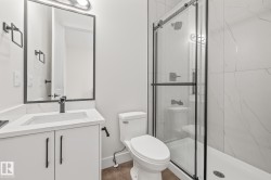 Modern bathroom featuring a glass-enclosed shower with white tiled walls, a white vanity with an integrated sink, a rectangular framed mirror, and matte black fixtures - 