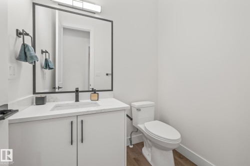 Bathroom featuring a white vanity with an integrated sink and matte black faucet, a large framed mirror, a white toilet, and wood-finish flooring - 132 Edgewater Circle, Leduc, AB 