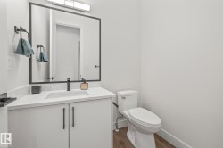 Bathroom featuring a white vanity with an integrated sink and matte black faucet, a large framed mirror, a white toilet, and wood-finish flooring - 