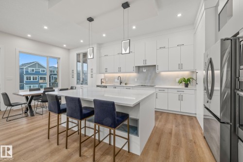 Spacious kitchen featuring an expansive island, white cabinetry, integrated stainless-steel appliances, and wood-finish flooring - 132 Edgewater Circle, Leduc, AB 