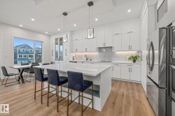 Spacious kitchen featuring an expansive island, white cabinetry, integrated stainless-steel appliances, and wood-finish flooring - 