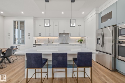 Kitchen featuring a large central island with a waterfall countertop, integrated stainless steel appliances, extensive white cabinetry, recessed lighting, and wood-finish flooring - 132 Edgewater Circle, Leduc, AB 
