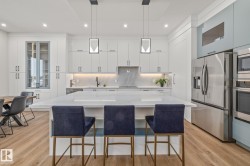 Kitchen featuring a large central island with a waterfall countertop, integrated stainless steel appliances, extensive white cabinetry, recessed lighting, and wood-finish flooring - 