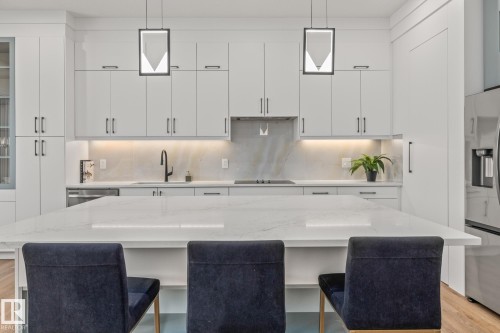 Gourmet kitchen featuring a substantial central island, sleek white cabinetry, under-cabinet lighting, a built-in cooktop, and contemporary pendant lighting fixtures - 132 Edgewater Circle, Leduc, AB 