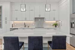 Gourmet kitchen featuring a substantial central island, sleek white cabinetry, under-cabinet lighting, a built-in cooktop, and contemporary pendant lighting fixtures - 