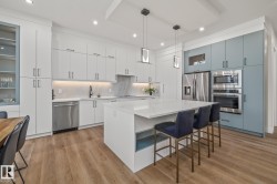 Spacious kitchen featuring an expansive island with a waterfall countertop, integrated stainless steel appliances, two-tone cabinetry, wood-finish flooring, and recessed lighting - 