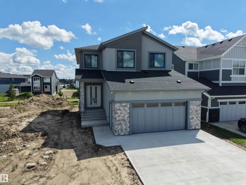Contemporary residential exterior featuring a two-car garage, concrete driveway, and stone veneer accents - 132 Edgewater Circle, Leduc, AB 