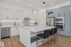 Gourmet kitchen featuring a large central island with seating, stainless steel appliances, white flat-panel cabinetry, a light-toned backsplash, and wood-finish flooring - 
