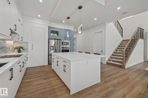 Modern kitchen featuring a large central island with a quartz countertop, white cabinetry with matte black hardware, stainless steel appliances, and wood-finish flooring - 132 Edgewater Circle, Leduc, AB 