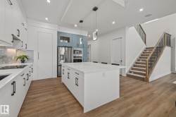 Modern kitchen featuring a large central island with a quartz countertop, white cabinetry with matte black hardware, stainless steel appliances, and wood-finish flooring - 