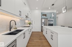 Gourmet kitchen featuring white cabinetry, a large center island with a stone countertop, an undermount double basin sink with a matte black faucet, integrated cooktop, and stainless steel appliances - 