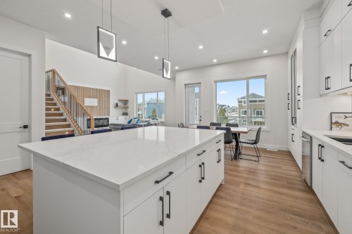 Open-concept living area with a large kitchen island featuring a white countertop and black hardware, wood-finish flooring, recessed lighting, and a modern staircase with wood treads and black railings - 132 Edgewater Circle, Leduc, AB 