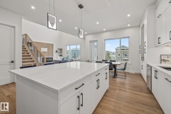 Open-concept living area with a large kitchen island featuring a white countertop and black hardware, wood-finish flooring, recessed lighting, and a modern staircase with wood treads and black railings - 