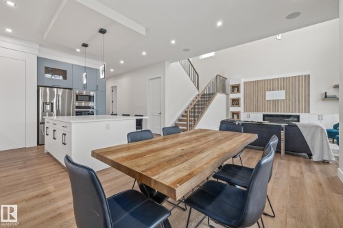 Open-concept living area featuring wood-finish flooring, a contemporary kitchen with stainless steel appliances, a spacious island with countertop seating, a staircase with metal railings, and a living room with a built-in fireplace and accent wall - 132 Edgewater Circle, Leduc, AB 