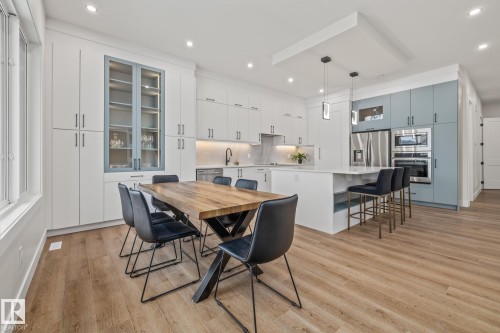 Modern kitchen featuring light wood-finish flooring, white and light blue cabinetry, stainless steel appliances, and a central island with pendant lighting - 132 Edgewater Circle, Leduc, AB 