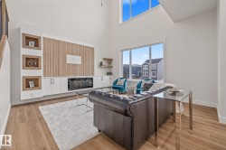 Spacious living area featuring wood-finish flooring, a built-in media console with an electric fireplace, custom wood-paneled wall accents, and high ceilings with upper windows - 