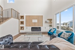 Spacious living area featuring high ceilings, large windows, wood-finish flooring, a contemporary fireplace, and built-in cabinetry with integrated shelving - 