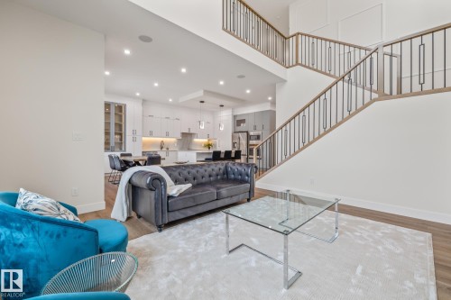 Two-story living area with wood-finish flooring, recessed lighting, and a prominent staircase featuring wood handrails and black metal balusters - 132 Edgewater Circle, Leduc, AB 