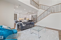 Two-story living area with wood-finish flooring, recessed lighting, and a prominent staircase featuring wood handrails and black metal balusters - 