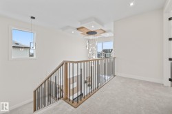 Upper-level hallway featuring a contemporary chandelier, recessed lighting, and a modern stair railing with wood-finish handrail and black metal balusters - 