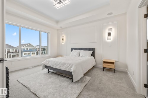 Spacious bedroom featuring large windows, tray ceiling, recessed lighting, and wall sconces - 132 Edgewater Circle, Leduc, AB 