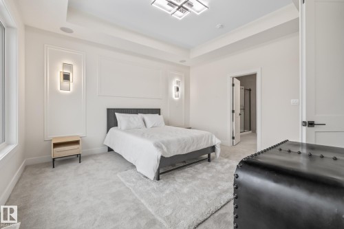 Recessed ceiling with an overhead light fixture, light gray carpeting, decorative wall molding, two wall sconces, and a window with white trim - 132 Edgewater Circle, Leduc, AB 