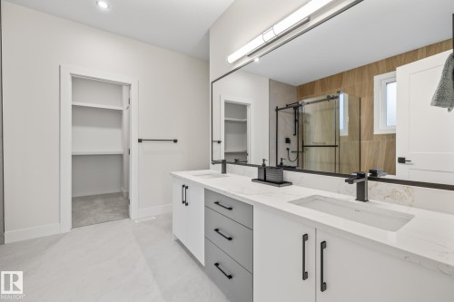 Contemporary bathroom featuring a double vanity with stone countertops, integrated sinks, and matte black fixtures - 132 Edgewater Circle, Leduc, AB 