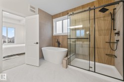 Contemporary bathroom featuring a freestanding soaking tub, a walk-in shower with matte black fixtures and a glass sliding door, and light wood-finish accent wall panels - 