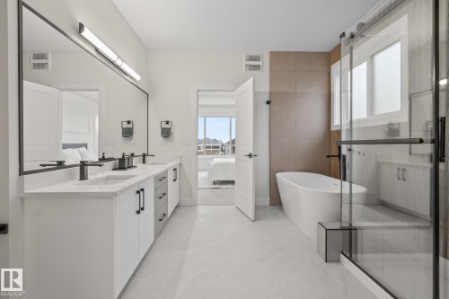 Contemporary bathroom featuring a freestanding soaking tub, a frameless glass shower enclosure, and a dual vanity with undermount sinks - 132 Edgewater Circle, Leduc, AB 