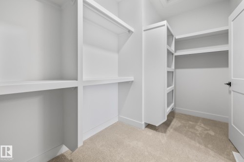 Walk-in closet featuring built-in shelving, hanging rods, an open-door entryway, and carpet flooring - 132 Edgewater Circle, Leduc, AB 